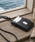 Porte-cartes zippé cuir noir posé sur un rebord de fenêtre face à la mer
