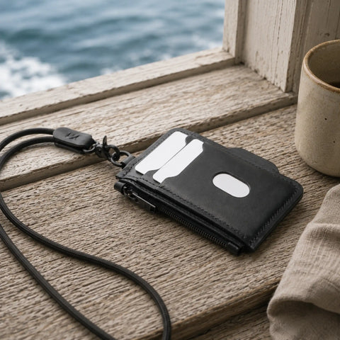 Porte-cartes zippé cuir noir posé sur un rebord de fenêtre face à la mer