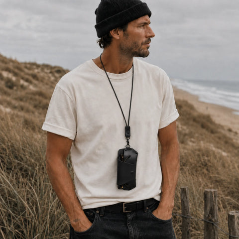 Homme portant un étui à lunettes cuir noir au cou, bord de mer